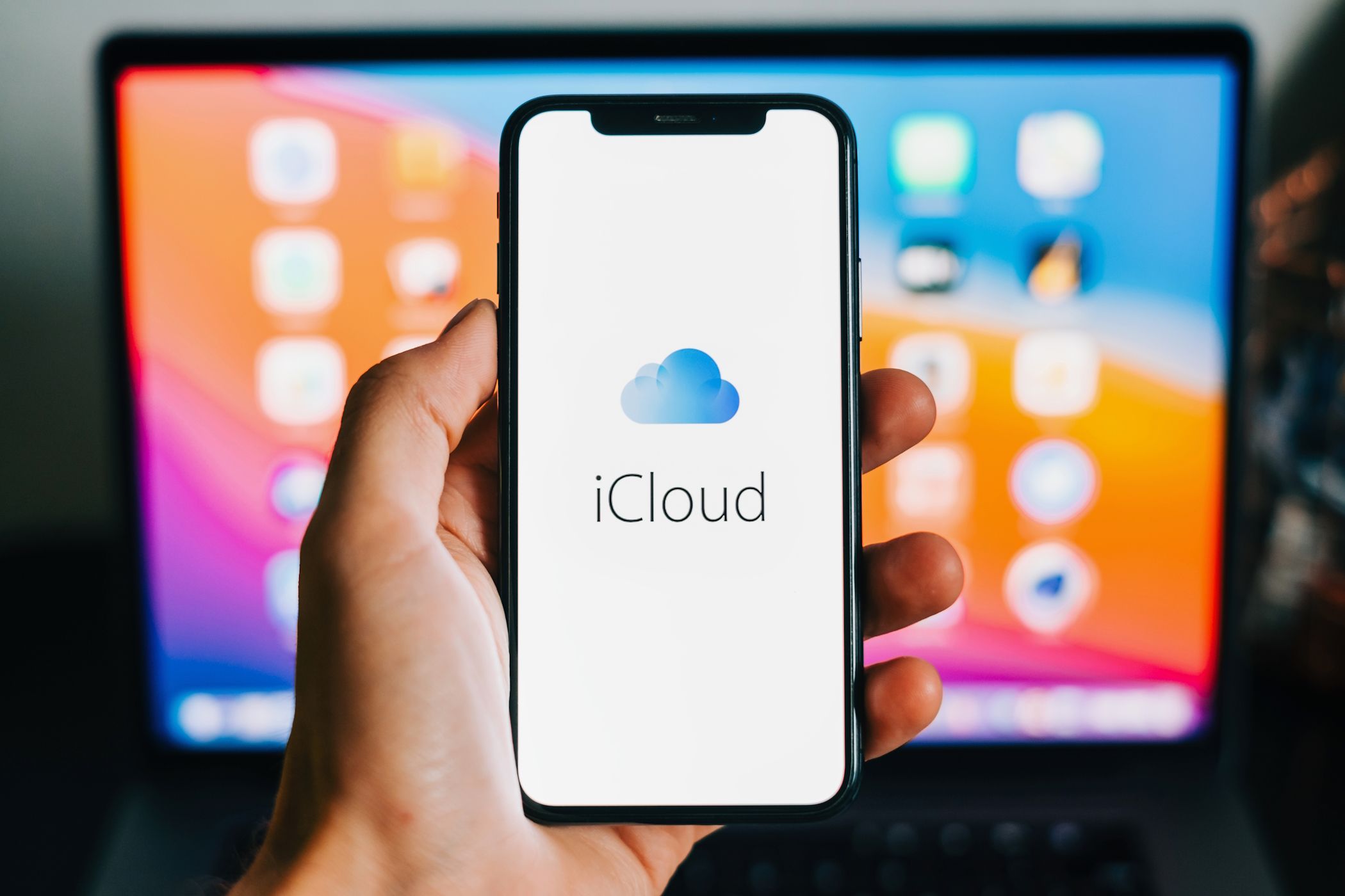 يظهر شعار iCloud على جهاز iPhone مع جهاز MacBook في الخلفية